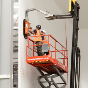 Workers using installing a large cold room panel with machinery